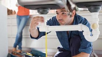 A plumbers works on sink drain under the counter